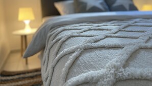 Un llit ben fet amb llençols i almoades blanques, una làmpada de nit i una finestra amb cortines.