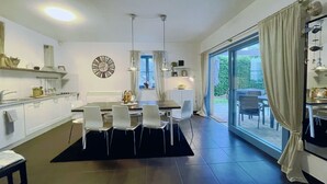 Una cuina moderna amb armaris blancs, una zona de menjador amb un rug negre i una gran porta corredissa de vidre que dona a un pati exterior.