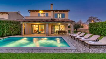 A two-story house with a swimming pool, outdoor seating, and a well-maintained garden.