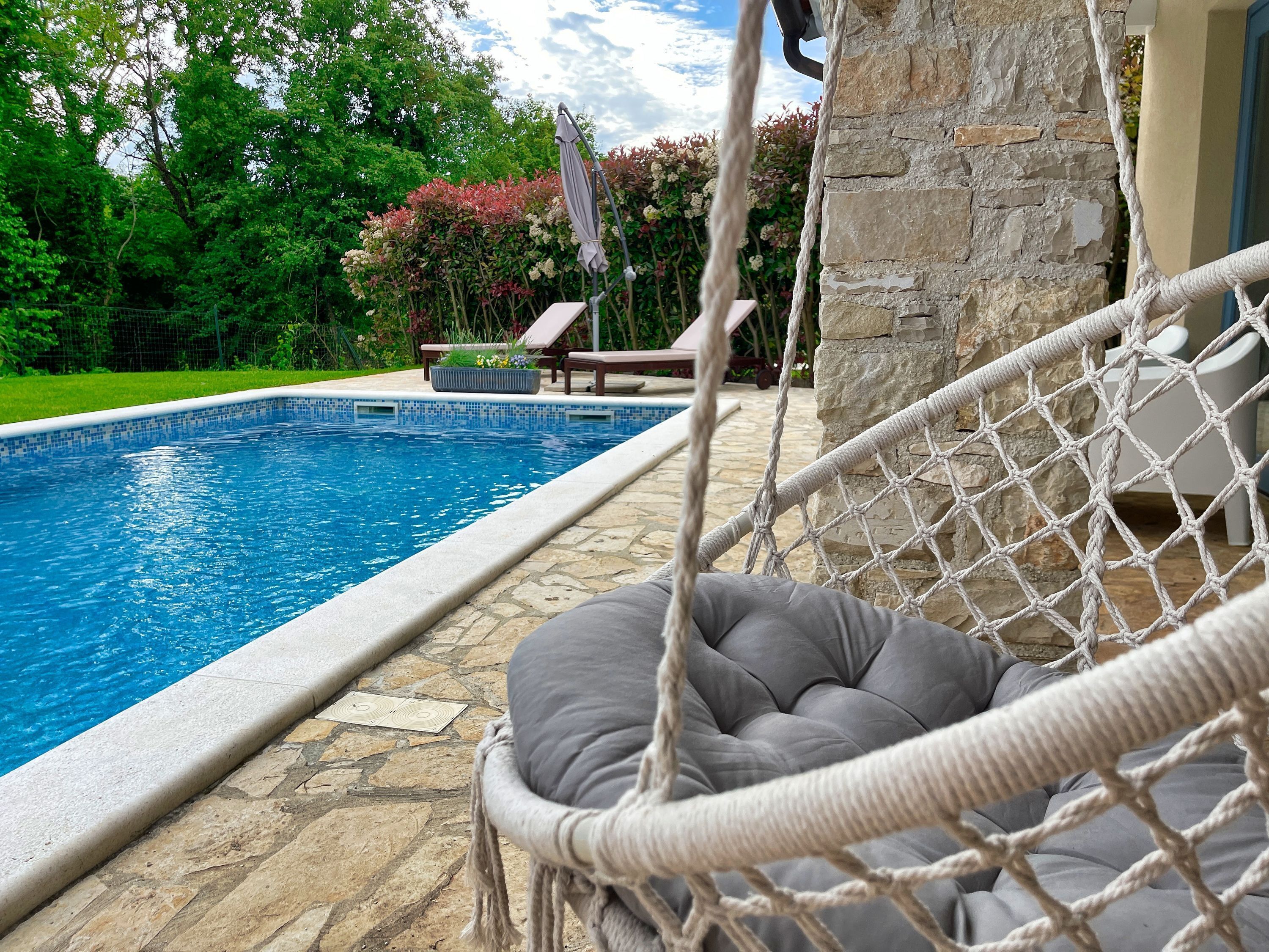 A poolside area with a hammock, a stone wall, and a lounge chair.