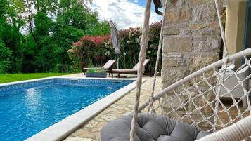 A poolside area with a hammock, a stone wall, and a lounge chair.