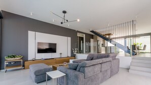 Una sala de estar moderna con un sofá seccional gris, un televisor de pantalla plana y una escalera de diseño minimalista.