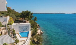 Uma propriedade costeira com piscina, degraus que levam à água e vista para o mar.