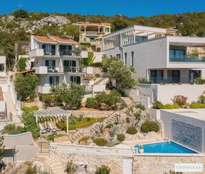 Um edifício residencial com vários andares, piscina, escadas de pedra e paisagismo exuberante.