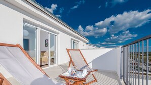 A balcony with two wooden lounge chairs, a small table with a glass container and cups, and a glass door leading to an interior room. - Dalmacija Viii in Suko an (Sukosan)