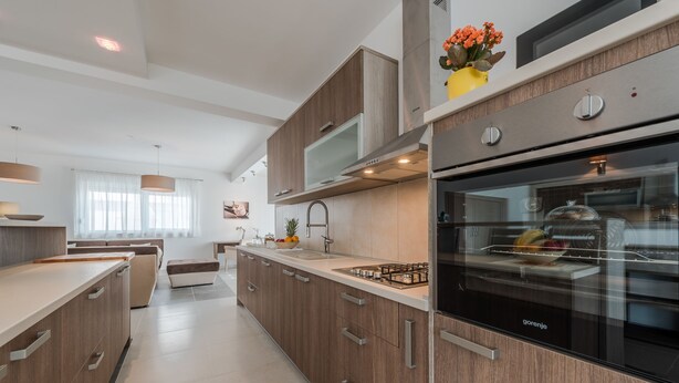 A modern kitchen with wooden cabinets, a built-in oven, and a large island with a sink. - Dalmacija Viii in Suko an (Sukosan)