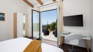 A bedroom with a bed, a desk with a chair, a TV, and a sliding glass door leading to an outdoor seating area with a view of the sky and greenery. - Dolce Bacio in Kavran (Marcana)