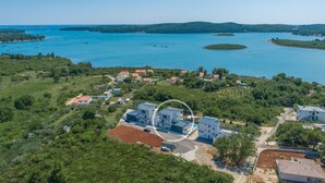 Une vue aérienne d’une zone côtière avec un ensemble de bâtiments, dont certains ont des toits rouges, entourés de verdure et bordée d’une grande étendue d’eau où se trouvent des bateaux.