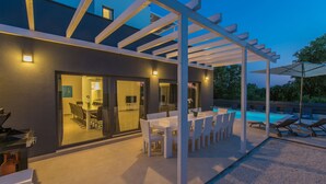 Une terrasse extérieure avec une piscine, des meubles blancs et un espace salon abrité.