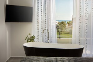A modern bathroom with a freestanding bathtub, a mounted TV, and a view of the outdoors through sheer curtains. - K in Premantura With 4 Bedrooms and 4 Bathrooms (Medulin)
