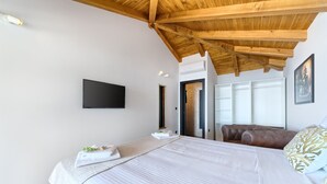 A bedroom with a wooden ceiling, a bed with white bedding, a flat-screen TV, and a brown leather sofa. - Filip in Murter With 4 Bedrooms and 2 Bathrooms (Tisno)