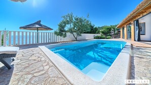 A swimming pool with a stone deck, a thatched umbrella, and a view of the sea. - Filip in Murter With 4 Bedrooms and 2 Bathrooms (Tisno)