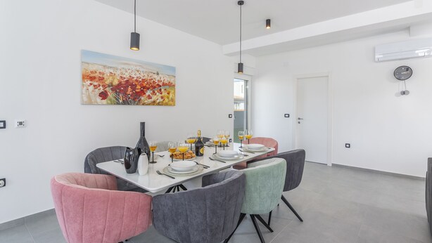 A modern dining area with a white table set for four, surrounded by colorful chairs, a painting on the wall, and a ceiling light fixture. - Elite 1 in Pula With 4 Bedrooms and 4 Bathrooms (Pula)