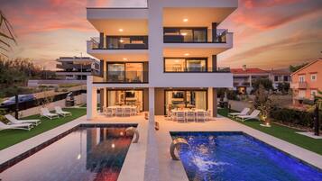 A modern two-story building with a swimming pool, outdoor seating, and a well-maintained garden.