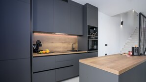 Uma cozinha moderna com armários escuros, bancada de madeira e forno embutido.