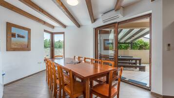 Un comedor amplio con una mesa y sillas de madera, ventanas grandes y un patio abierto con mobiliario exterior.