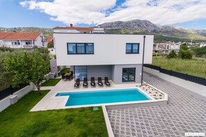 A modern two-story house with a swimming pool, outdoor seating, and a view of the surrounding landscape. - Kastel One in K Kambelovac (Kastela)