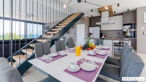 Un espace de salle à manger moderne avec une table dressée pour quatre personnes, un escalier et une cuisine en arrière-plan.