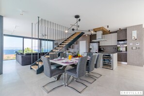 A modern kitchen with a built-in wine cooler, a dining area with a table set for four, and a staircase leading to a balcony with a city view. - Vitae in Sutivan With 3 Bedrooms and 3 Bathrooms (Sutivan)