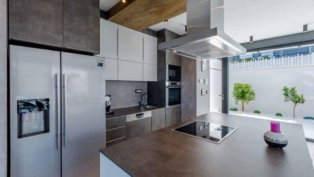 Une cuisine moderne dotée d’appareils électroménagers en acier inoxydable, d’un four encastré et d’un grand îlot central avec un plan de travail en verre.