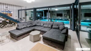 Un salon moderne doté d’un grand canapé d’angle, d’une table basse et offrant une vue sur une piscine intérieure grâce à de grandes portes vitrées.