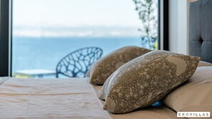 Une chambre à coucher avec un lit, des coussins à motifs, une vue sur la mer et un fauteuil.