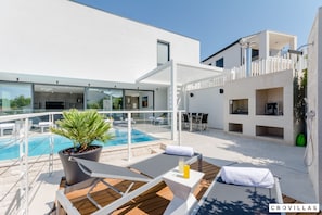 A modern outdoor pool area with lounge chairs, a potted plant, and a glass-enclosed room. - Vitae in Sutivan With 3 Bedrooms and 3 Bathrooms (Sutivan)