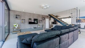 Un salon moderne doté d’un grand canapé d’angle, d’un téléviseur à écran plat et d’un escalier menant à un niveau supérieur.