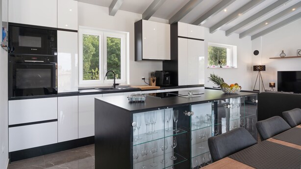 Een moderne keuken met witte kasten, een zwart eiland met glazen deuren en een geïntegreerde wijnkoeler.