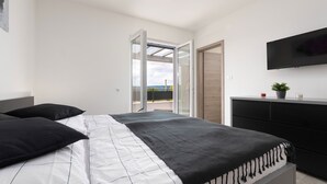 Een slaapkamer met een bed, een dressoir, een televisie en een balkon met uitzicht.