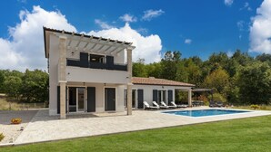 Een twee verdiepingen tellend huis met een zwembad, een overdekt terras en een verzorgd gazon.