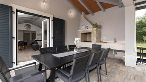 Een buiten eethoek met een zwarte tafel en stoelen, een pergola erboven en een keuken met een gootsteen en aanrecht.