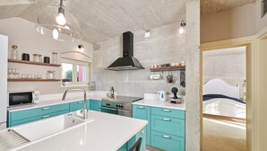 A modern kitchen with a central island, stainless steel appliances, teal cabinetry, and a large black range hood. - Mediterranea in Umag (Umag)