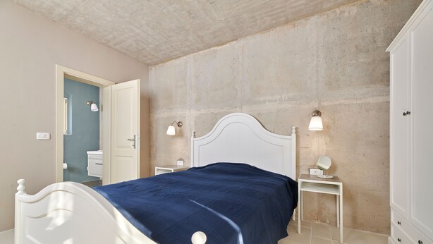 A bedroom with a white bed, a blue bedspread, two bedside tables with lamps, a small mirror, and a wardrobe. - Mediterranea in Umag (Umag)