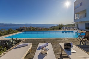 Un área junto a la piscina con sillones de descanso, una computadora portátil y un sombrero de sol.
