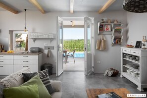Een moderne keuken met witte kasten, een eethoek met een tafel en stoelen, en een zwembad zichtbaar door een open deur.