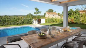 Ein Essbereich im Freien mit Pool, Korbmöbeln und Blick auf die Landschaft.
