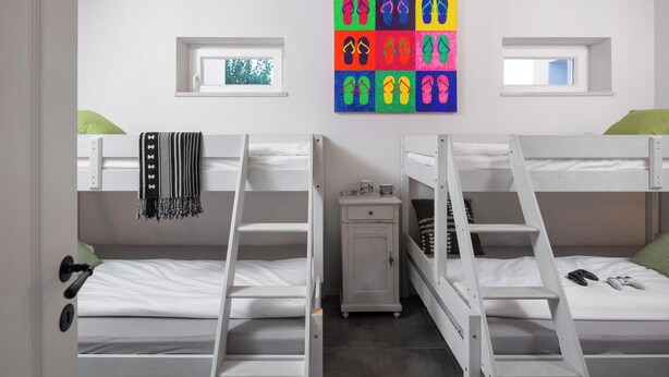 Ein Schlafsaalzimmer mit Etagenbetten, einem kleinen Schrank und einem farbenfrohen Bild an der Wand.