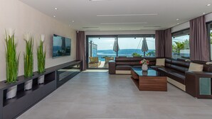 A modern living room with a large flat-screen TV, a sofa, a coffee table, and a balcony with a view of the sea. - Lorena Crikvenica in Crikvenica (Crikvenica)