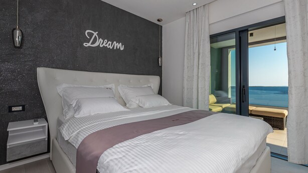 A modern bedroom with a large bed, a dark textured wall with the word "Dream" written on it, and a view of the sea through a sliding glass door. - Lorena Crikvenica in Crikvenica (Crikvenica)