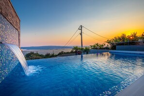 A swimming pool with a tiled edge, a waterfall feature, and a view of the sunset over the water. - Lorena Crikvenica in Crikvenica (Crikvenica)