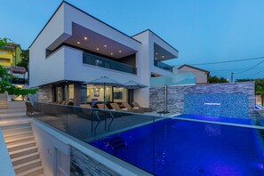 A modern two-story house with a glass-enclosed swimming pool, outdoor seating, and a stone wall. - Lorena Crikvenica in Crikvenica (Crikvenica)