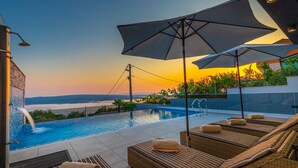 A rooftop infinity pool with lounge chairs and umbrellas, overlooking a sunset and a distant shoreline. - Lorena Crikvenica in Crikvenica (Crikvenica)
