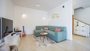 A modern living room with a teal sofa, a small coffee table, a TV, and a guitar. - Dija in Jur i i With 3 Bedrooms and 3 Bathrooms (Svetvincenat)