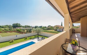 Un balcón con piscina, mobiliario exterior y vistas a un jardín y casas.