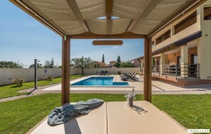 Un área de piscina con sillones de descanso y una pérgola.