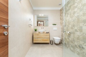 Un baño moderno con tocador de madera, un lavabo blanco y cabina de ducha de vidrio.