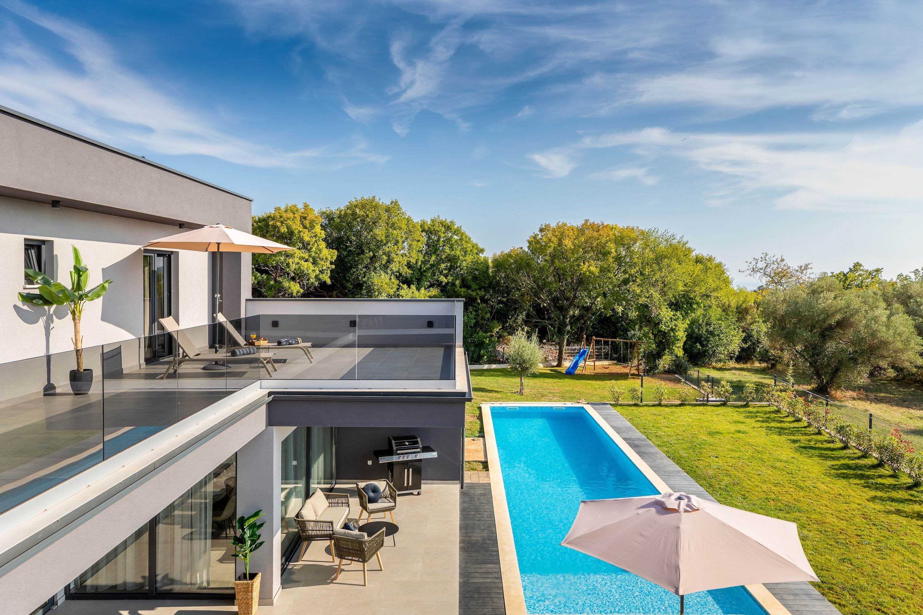 Ein modernes, zweistöckiges Haus mit einem Glasbalkon, einem Schwimmbad und einem gepflegten Garten.
