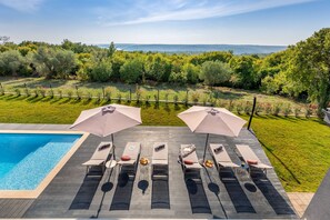 Zona de piscina con sillones de descanso y sombrillas, un muelle de madera y vistas a un paisaje exuberante.