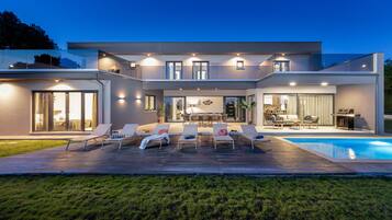 Ein modernes Haus mit Pool, Sitzgelegenheiten im Freien und einer gut beleuchteten Terrassenfläche.